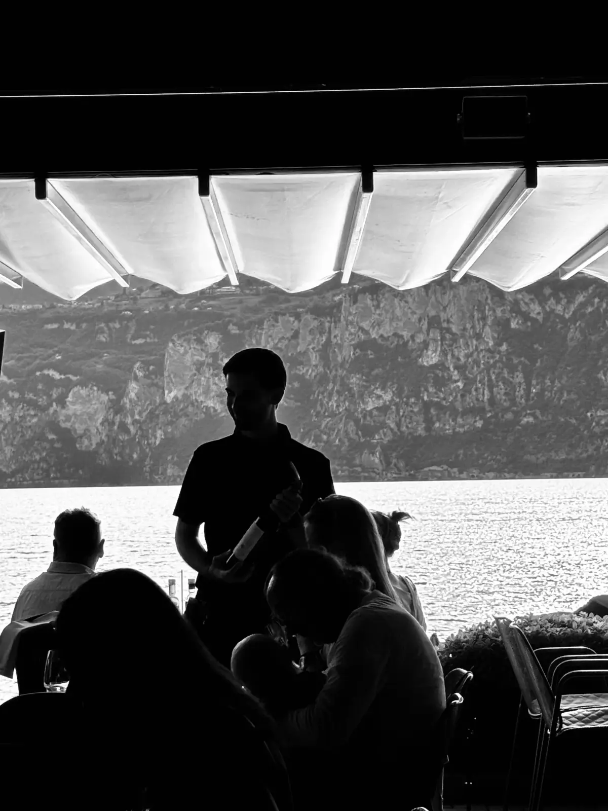 Cameriere che serve il vino ai tavoli affacciati sul lago, in bianco e nero