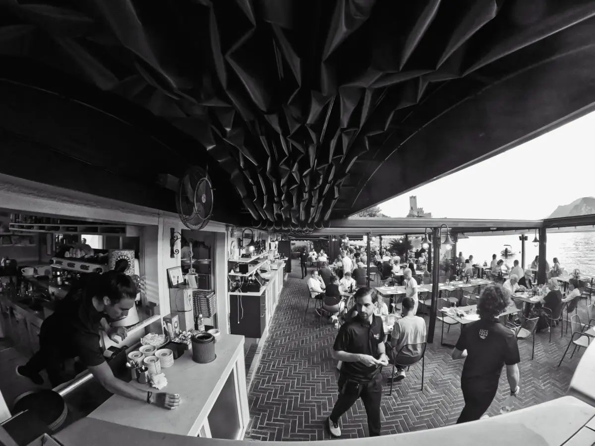 Panoramica in bianco e nero della sala e della terrazza del Lido Paina piene di ospiti